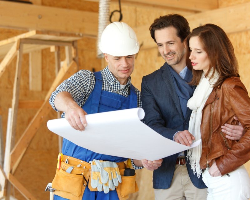 a builder shows a smiling man and woman blueprints