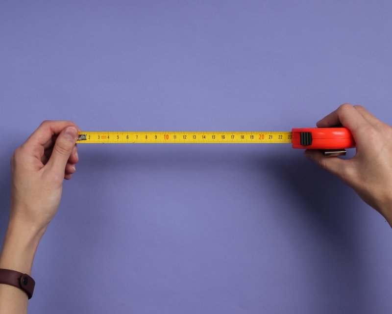 hands hold a metal tape measure with a foot of tape extended, purple background
