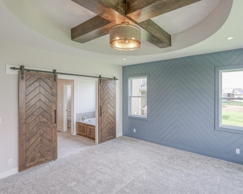 an empty room with wood, chevron-patterned, sliding barn doors leading to an ensuite bathroom